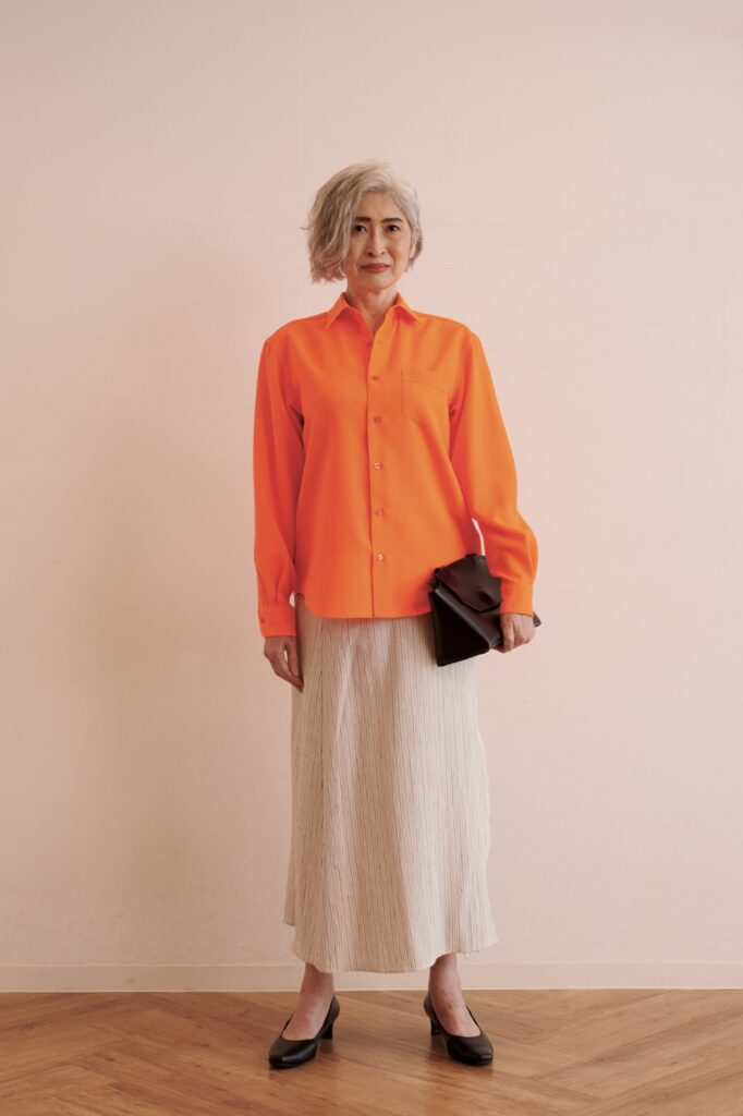 オレンジのシャツにベージュのロングスカートの女性